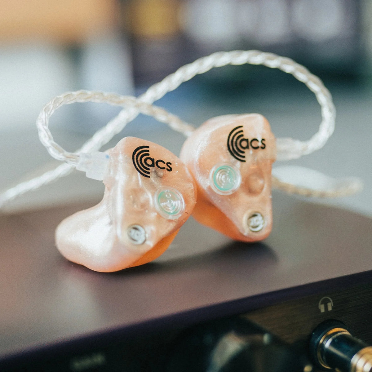 Pair of ACS in-ear monitors on a surface with a blurred background