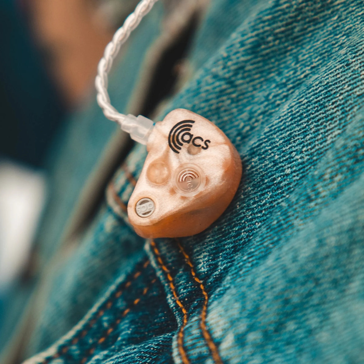 Close-up of a hearing aid on a person's pocket with 'acs' branding.