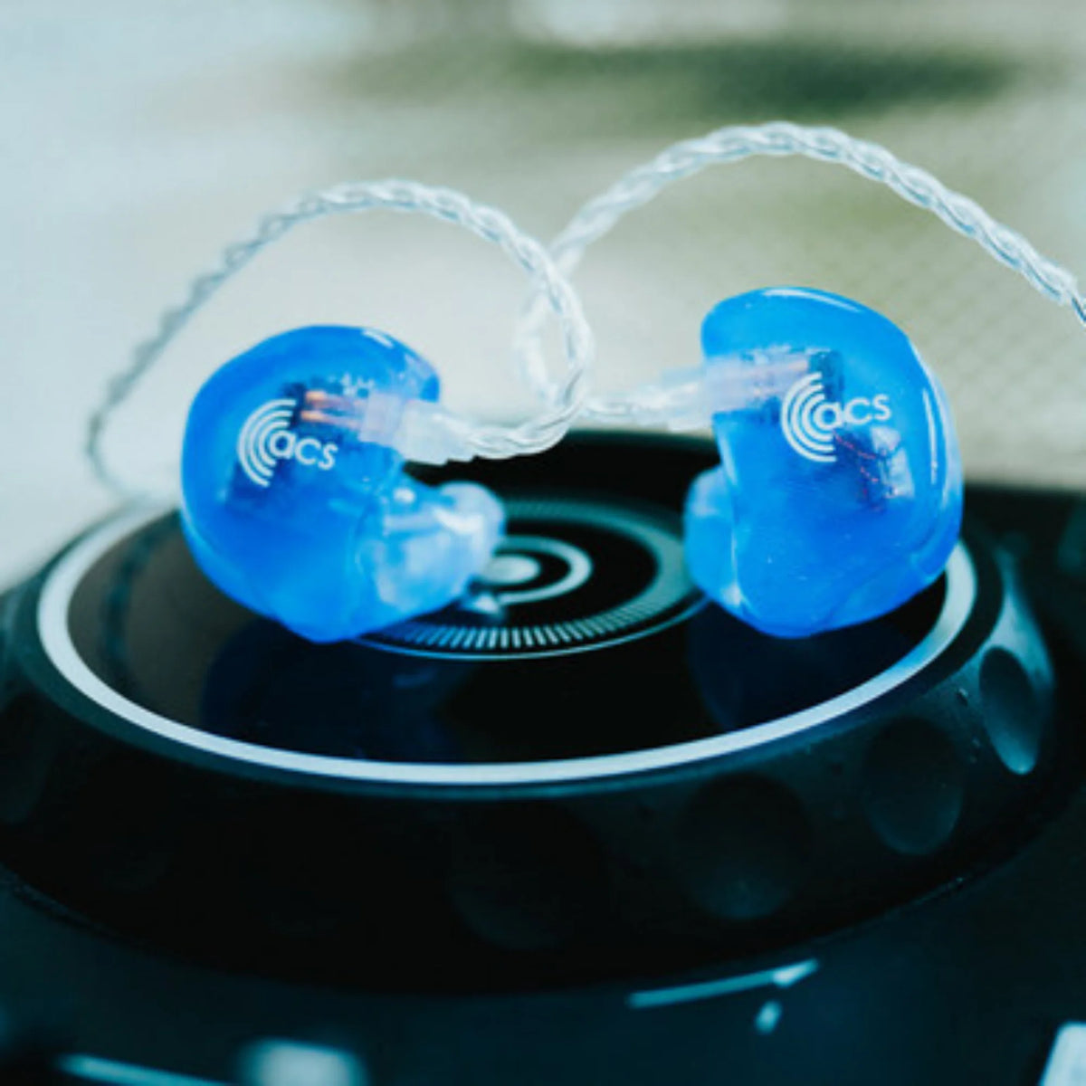 Blue earbuds with 'acs' logo on a black surface