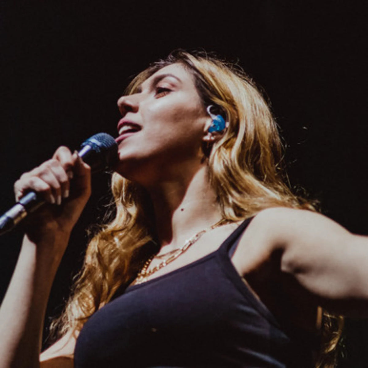 Woman singing into a microphone with a dark background