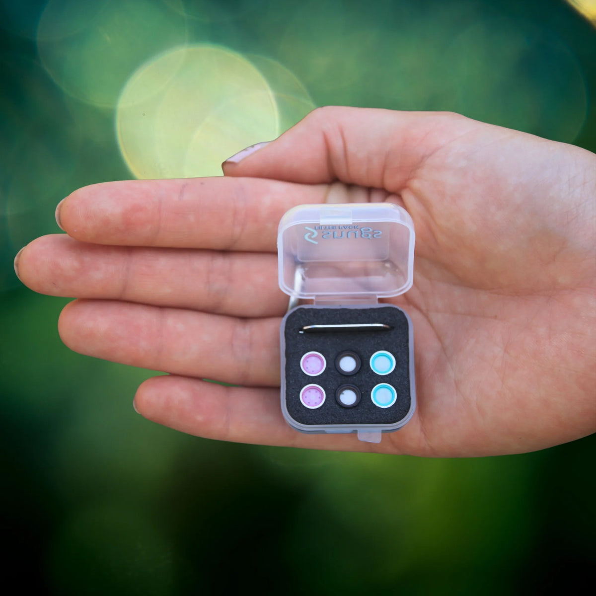 Hand holding a small earplug filters  against a blurred green background