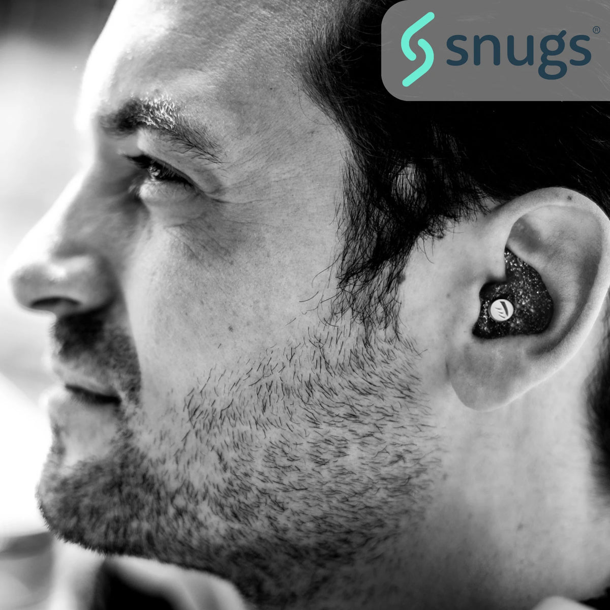 Close-up of a person wearing an earplug with 'snugs' logo.
