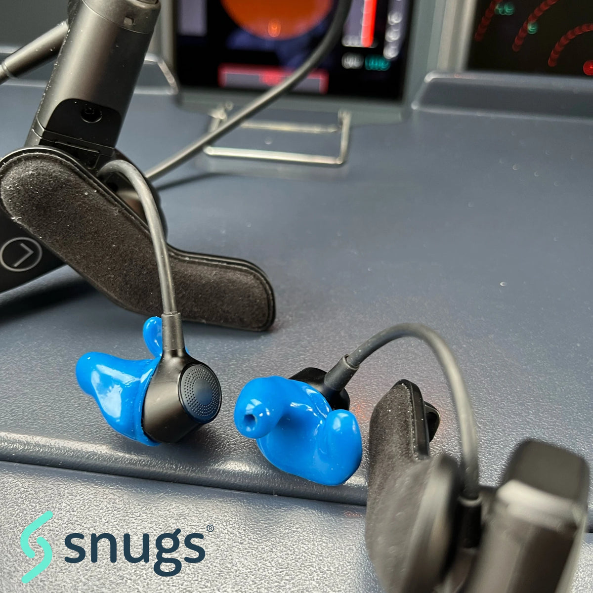 blue earplugs on aviation headset sitting on desk with snugs logo in background