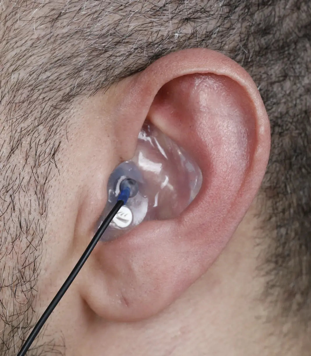 human ear with clear earplug in with filter and cable attached
