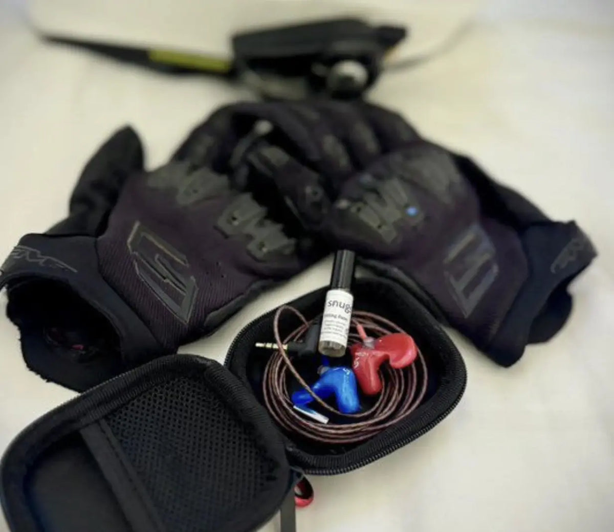 earplugs in black carry case and set of motorcycle gloves next to them