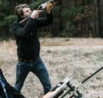 Man in outdoor setting holding a shotgun with a blurred background