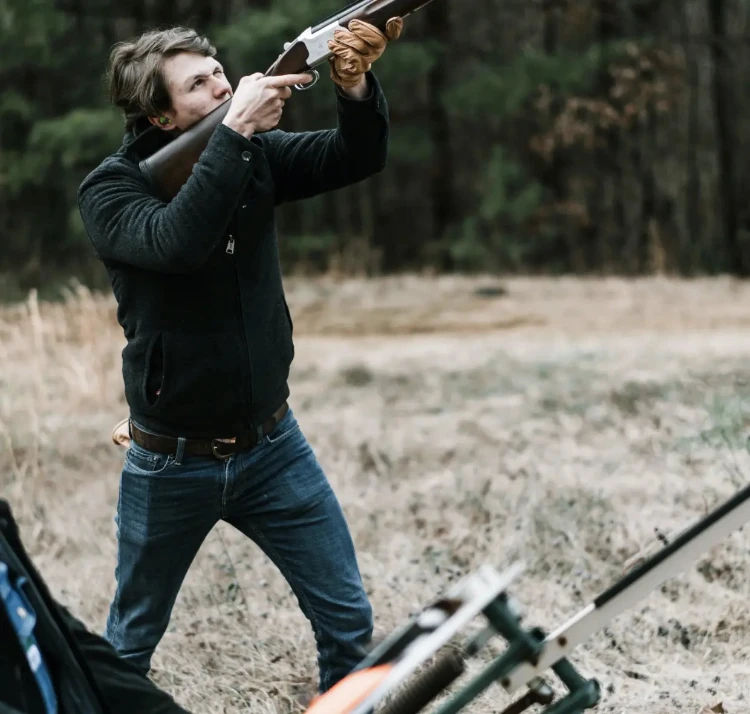 Man in outdoor setting holding a shotgun with a blurred background