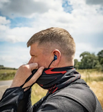 Man adjusting a neck gaiter with a blue earplug outdoors