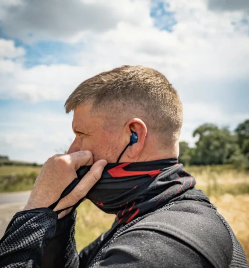 Man adjusting a neck gaiter with a blue earplug outdoors