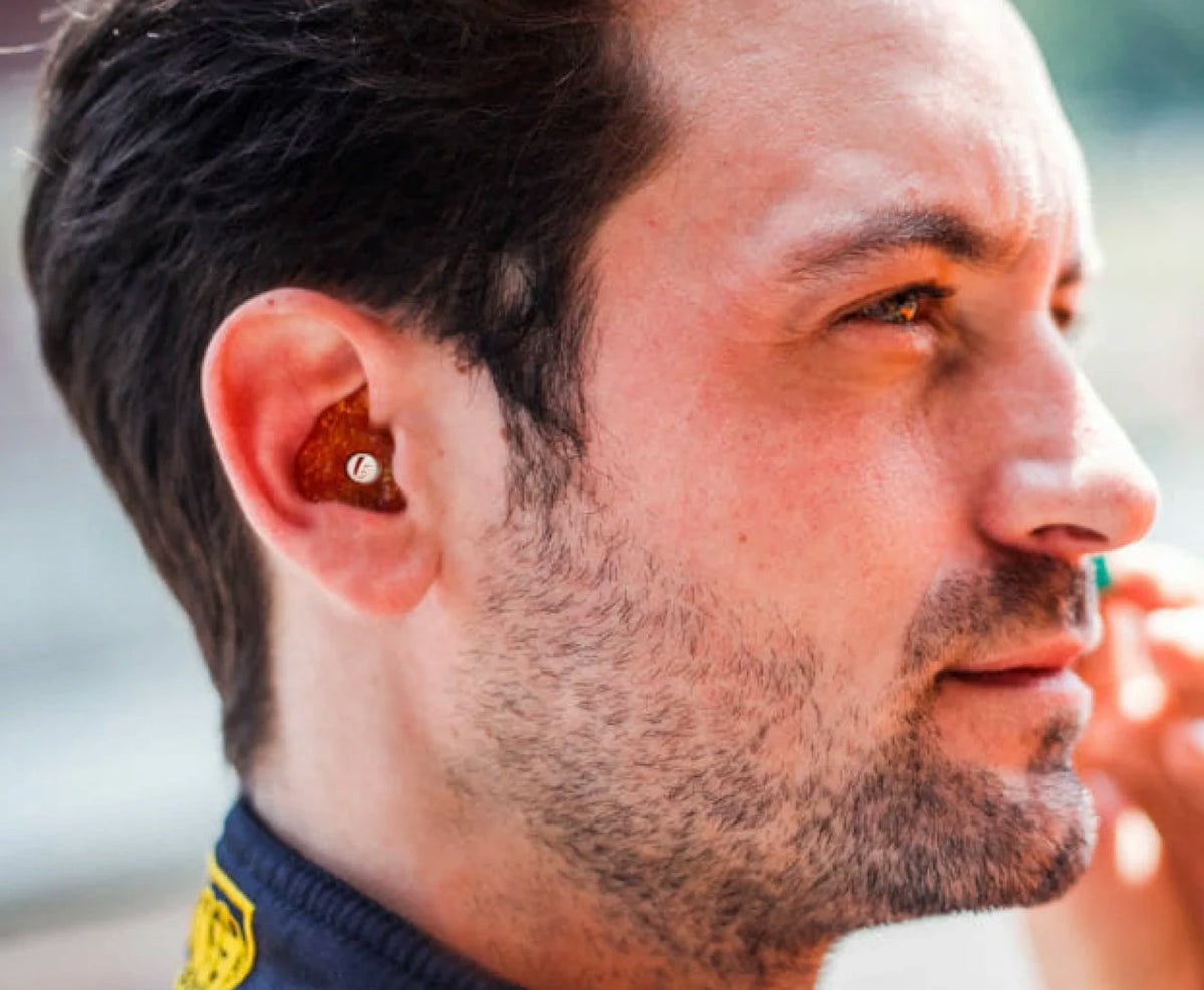 Close-up of a man with earplugs in his ear, wearing a dark shirt.