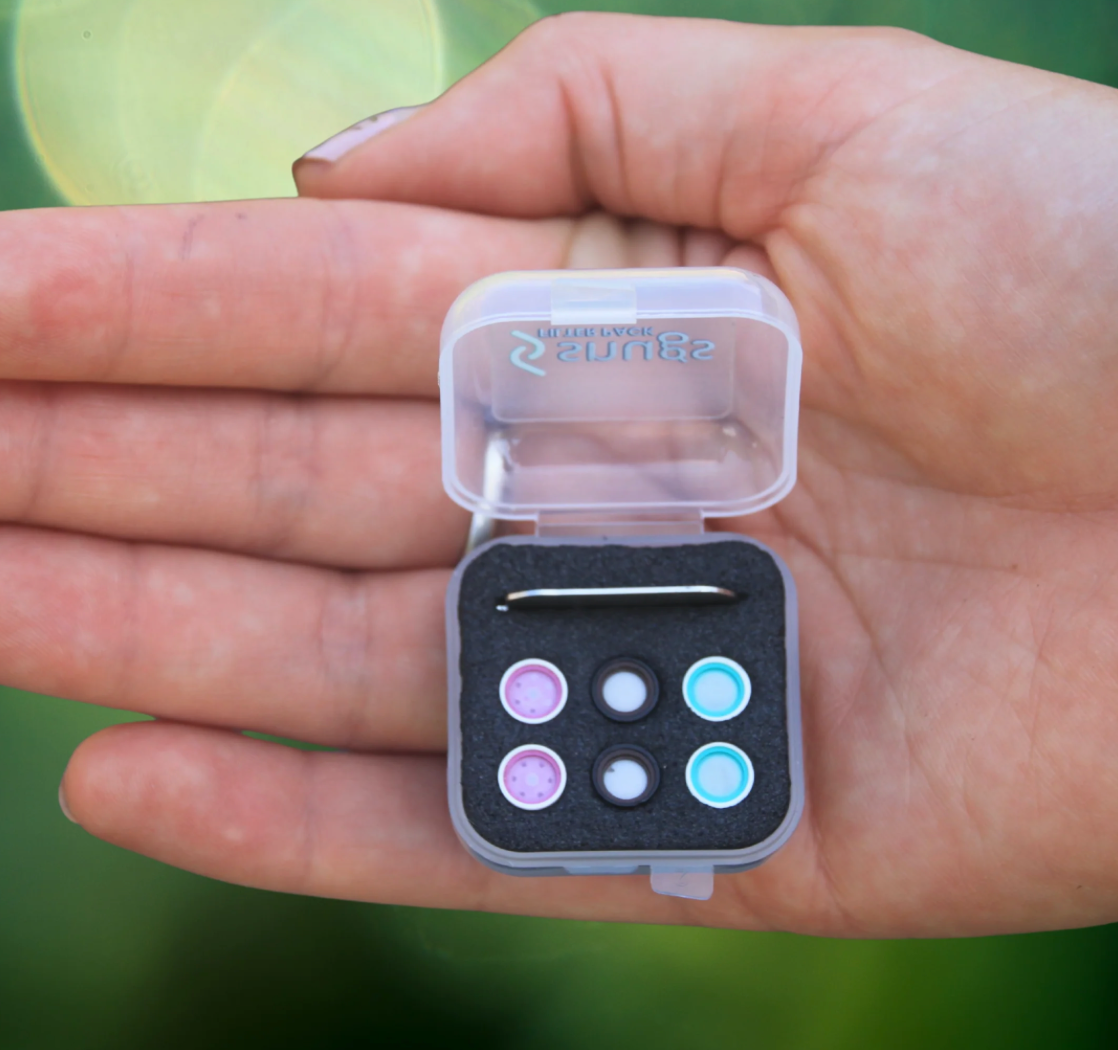 Small container with colorful beads and a needle held in a hand against a blurred green background