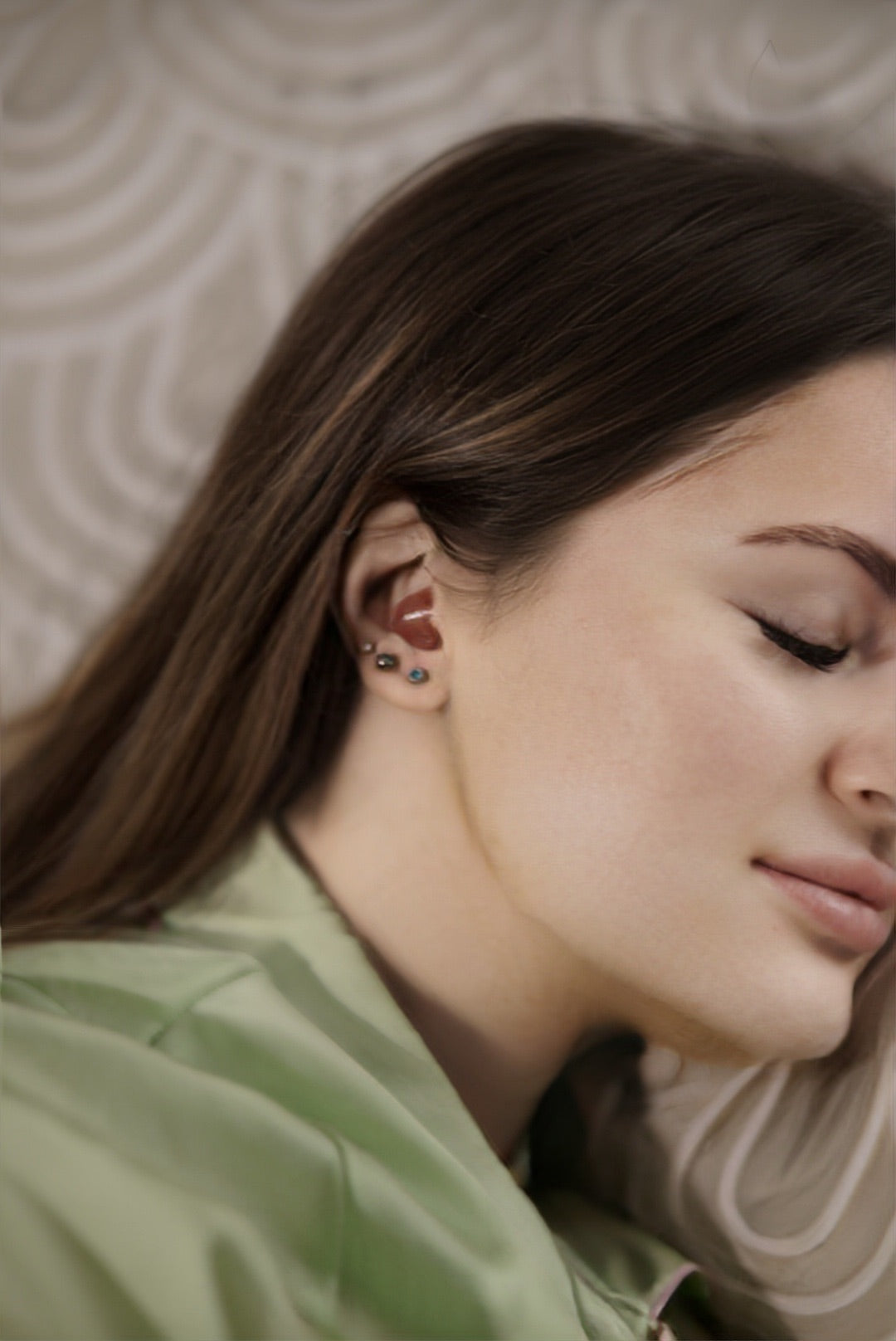 lady sleeping wearing green tip and has brown hair with red earplugs in her ears